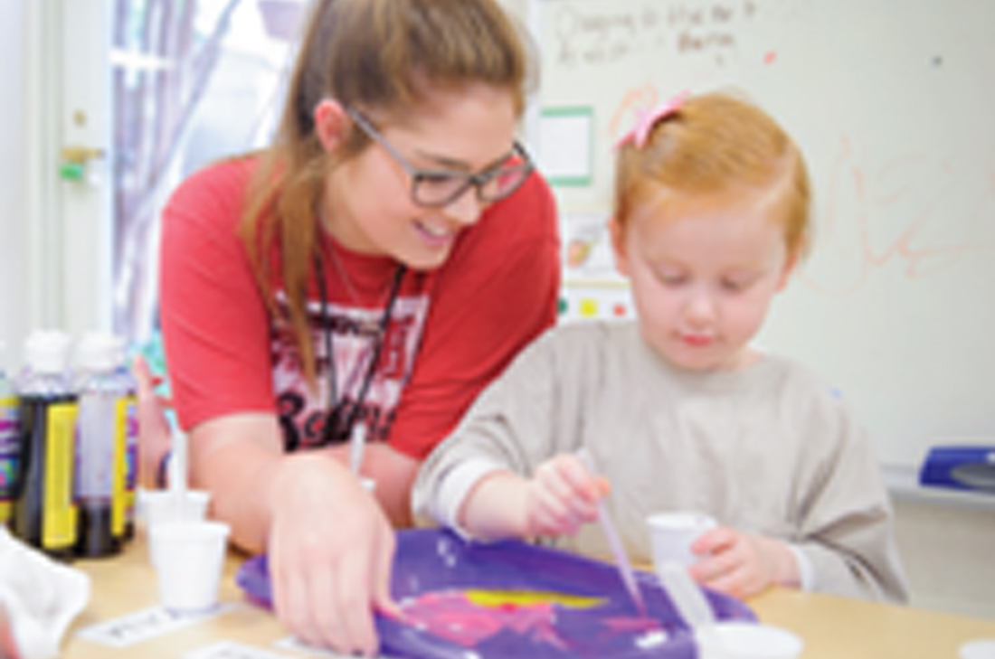 a student teacher helps a young child paint