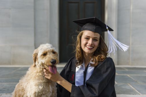 a student in graduation regalia and her dog