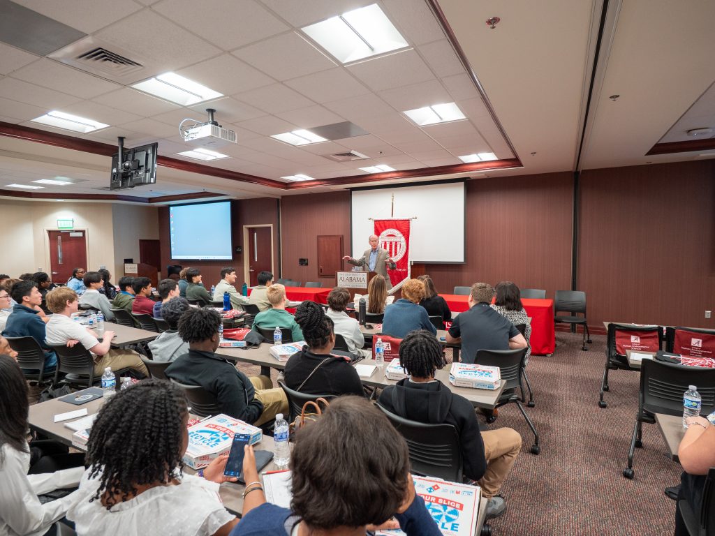 Man at a podium speaks to a group of high school students